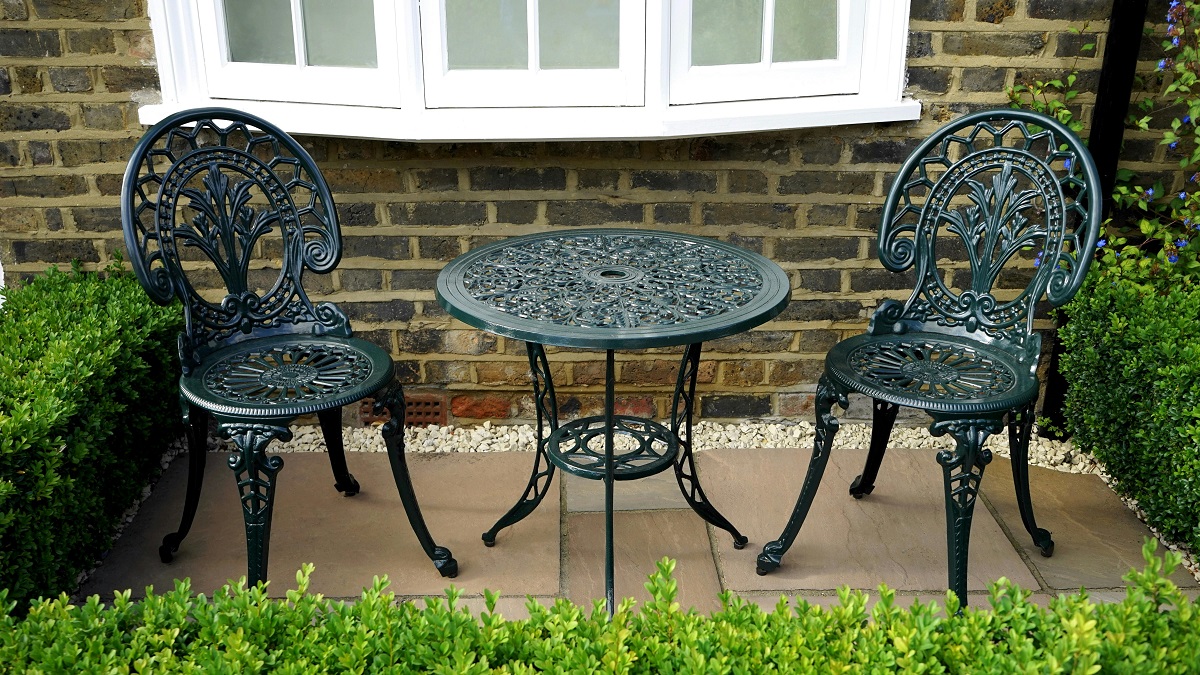 patio table and chairs encircled by bushes, with a brick wall behind 